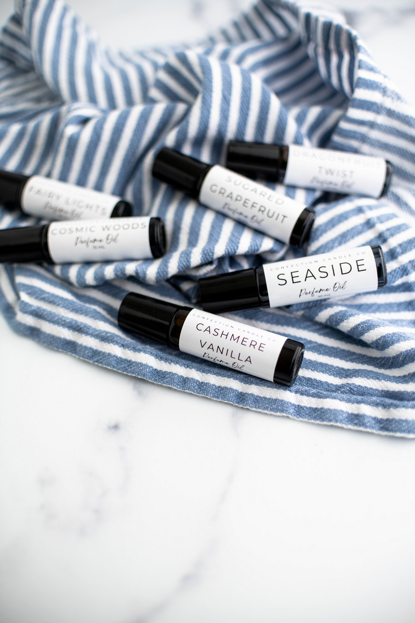 Variety of amber glass roller bottle perfume oils laying on a blue and white striped kitchen towel.